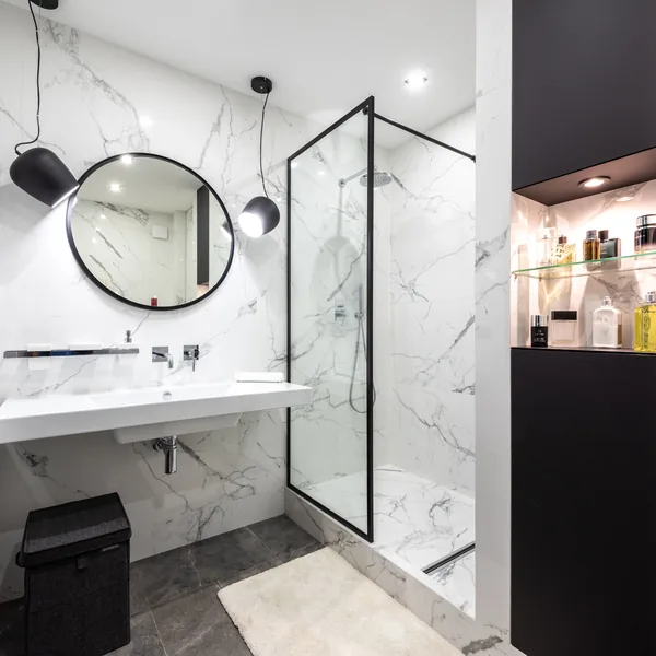 Remodeled Findlay bathroom with a marble wet wall, glass shower panel, floating vanity and round mirror