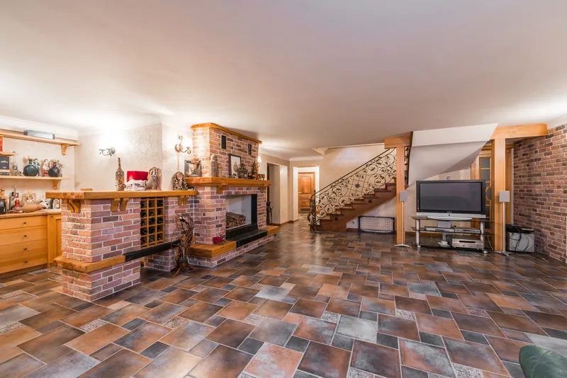 Dated finished basement with a brick fireplace, built-in bar, and patterned tile floor awaiting an update