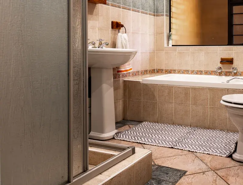 Dated bathroom with beige wall tile, a decorative border strip, pedestal sink, and a tiled tub apron awaiting renovation