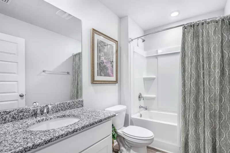 White bathroom with a granite vanity top and an alcove tub behind a curtain