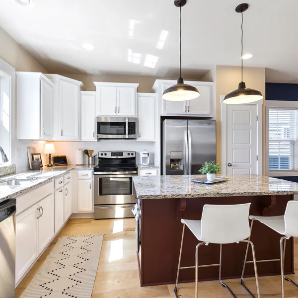 White perimeter cabinets with a contrasting island and pendant lights in a remodeled kitchen