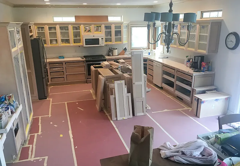Kitchen mid-installation with cabinet boxes staged and the floor covered for protection