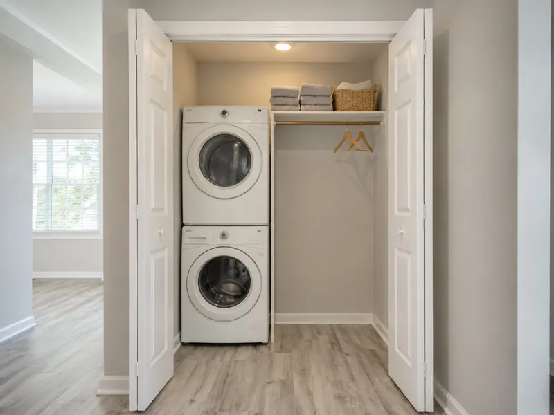 Laundry closet with a stacked washer and dryer, a shelf of folded towels above, and a hanging rod behind open bifold doors