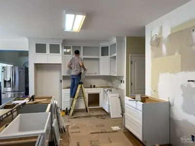 In-house remodeling crew member on a ladder finishing cabinetry inside a home under renovation