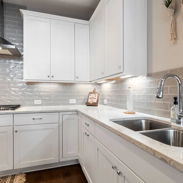 Grey subway tile backsplash running between the counter and upper cabinets around a kitchen sink
