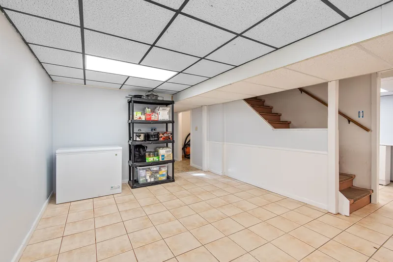 Unfinished basement with exposed framing, a drop ceiling, and open stairs before remodeling